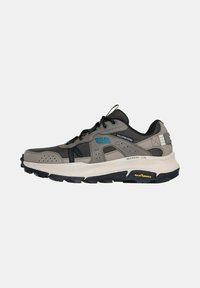 Scarpa sportiva grigia e nera con logo blu, pannelli in rete, suola spessa bianca e battistrada Goodyear, vista laterale su sfondo bianco.