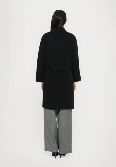 Black long coat with a straight cut, wide sleeves, and a belted waist, paired with grey wide-leg checked trousers. Textured fabric finish.