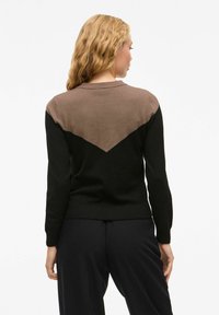 Pull en tricot noir et marron avec un motif en chevron au dos, des poignets côtelés et un col rond. Texture douce avec une silhouette ajustée.