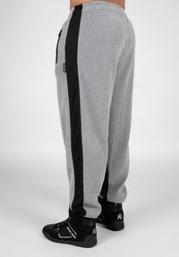 Grijze geribbelde sweatpants hebben zwarte zijstroken en een trekkoord in de taille, gecombineerd met zwarte sportschoenen. Geen zichtbare logo's of patronen.