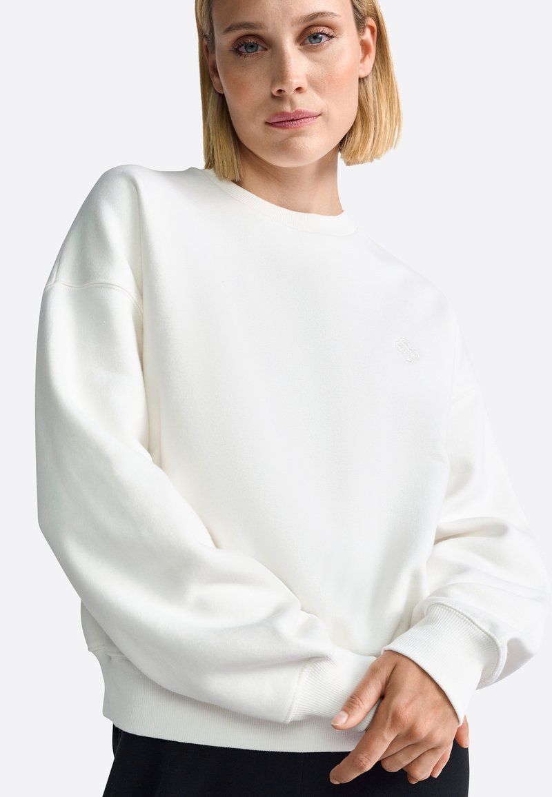 Sudadera de algodón blanca con cuello redondo, hombros caídos y puños acanalados. Presenta un sutil logotipo bordado en el pecho.
