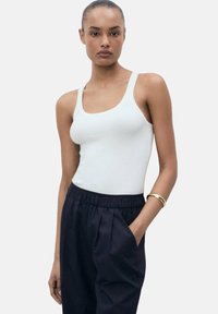 Geribbeld witte tanktop met een ronde hals en brede schouderbanden, gedragen met donkerblauwe broeken met een relaxte pasvorm en zijzakken.