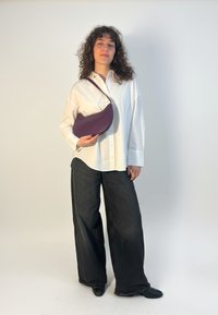 Fialová kožená kabelka s oblým dizajnom, doplnená bielou košeľou na gombíky a čiernymi širokými nohavicami. Minimalistický štýl.