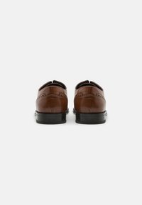 Zapatos de cuero marrón con un acabado suave, que presentan una punta redondeada y una suela de goma negra duradera. La vista trasera resalta el detalle de la costura.