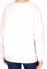 Vaaleanharmaa, ylisuurikokoinen svetaritakki, jossa on roikkuvat olkapäät, ribbetyt hihansuut ja pehmeä tekstuuri. Näkyvät saumat ja suora helma takana.