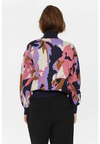 Megztinis su daugiaspalviu abstrakčiu raštu, kuriame dominuoja violetinė, rožinė ir ruda; krakmolyti apykaklės ir rankovių detalės.