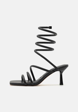 Sort højhælet sandal med tynde stropper og en spiralformet ankelrem med tekstureret finish og kvadratisk åben tå.