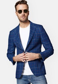 Niebieska marynarka w kratę o dopasowanym kroju, z czerwonymi i żółtymi akcentami, zapinana na pojedynczy guzik, z teksturowanej tkaniny. Noszona na białej koszulce.