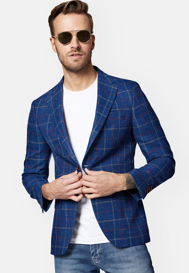 Niebieska marynarka w kratę o dopasowanym kroju, z czerwonymi i żółtymi akcentami, zapinana na pojedynczy guzik, z teksturowanej tkaniny. Noszona na białej koszulce.