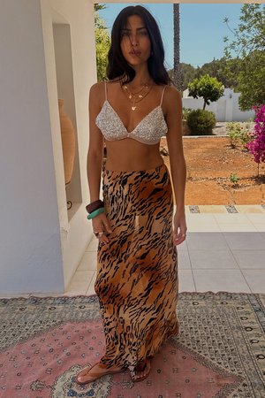 Beaded bralette in silver with light fabric; flowing maxi skirt in animal print with orange and black stripes; brown sandals, layered bracelets.