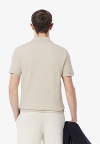 Beige piké med korta ärmar, tillverkad av mjukt stickat tyg. Har en klassisk krage och rak fåll. Bärs med ljusa byxor.