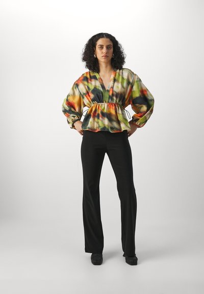Bluză multicolor cu decolteu în V, talie strânsă și mâneci bufante, realizată dintr-un material ușor. Asortată cu pantaloni negri evazați și pantofi închisi la culoare.