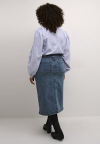 Falda de mezclilla azul con un corte recto, de diseño hasta la mitad de la pierna, que cuenta con bolsillos traseros. Combinada con una blusa a rayas azul y blanca.