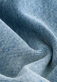Heledsinine denimkangas, millel on peen tekstuur. Materjalil on diagonaalsed sooned ja peened värvitoonide varieerumised.