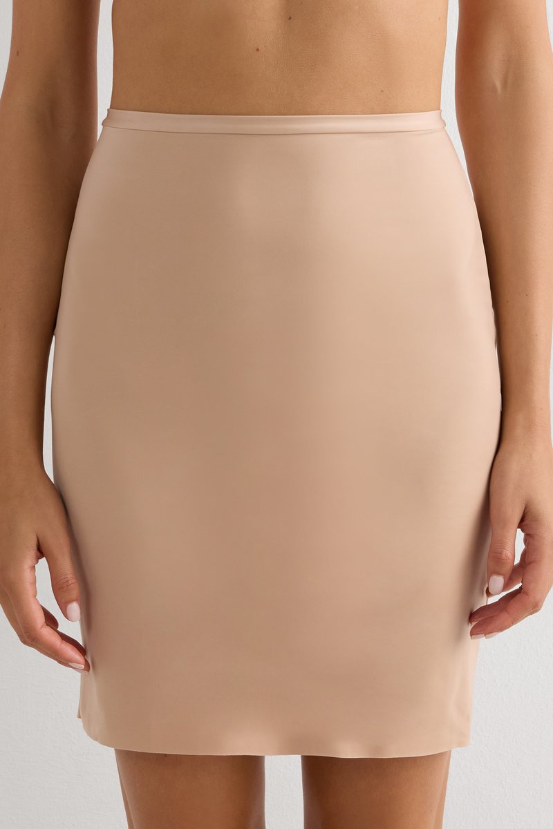 Femme portant une jupe crayon beige taille haute, longueur genou, avec une texture lisse, debout devant un fond clair.