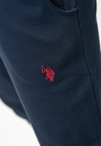 Marineblauwe sweatpants van katoen, met een rood geborduurd logo op het dijgebied. Zachte textuur met een casual ontwerp.