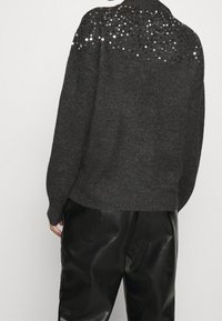 Grå stickad tröja med en paljettdekoration på axlarna, kombinerad med svarta läderbyxor. Tröjan har en avslappnad passform och ribbat nederkant.