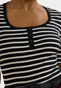 Pruhovaný černobílý top s kulatým výstřihem a tříknoflíkovou légou. Měkká textura, přiléhavý střih a krátké rukávy.