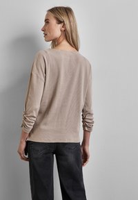 Top a maniche lunghe a righe beige con vestibilità morbida, caratterizzato da polsini arrotolati e un ampio scollo, abbinato a jeans grigio scuro.