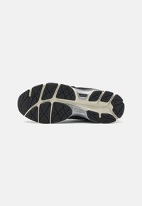Semelle de chaussure de course noire avec une semelle extérieure en caoutchouc texturé, dotée d'un intercalaire blanc et d'un motif de bande de roulement géométrique pour une traction optimale.