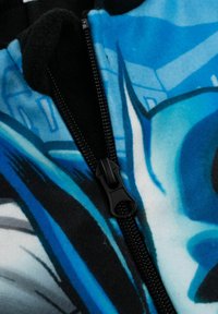 Tuta in pile con un design grafico blu e nero. Dotata di una cerniera nera sul davanti. Tessuto morbido con contrasti di colore vivaci.