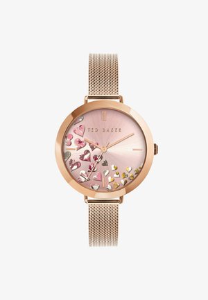 Zegarek na różowo-złotym mesh strapie z różowym cyferblatem ozdobionym metalicznymi sercami i złotymi akcentami, z minimalistycznymi wskaźnikami godzin i wskazówkami.