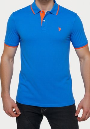 Mann trägt ein blaues Poloshirt mit kurzen Ärmeln und orangefarbenem Besatz an Kragen, Ärmelsäumen und Knöpfen, kombiniert mit schwarzen Hosen.