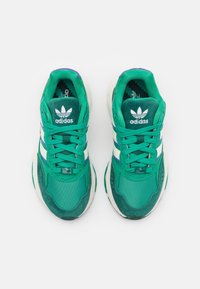 Un paio di sneakers verdi Adidas con strisce bianche, lacci allacciati, logo del brand visibile sulla linguetta e suole imbottite, viste dall'alto.