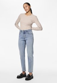 Chemise à rayures à manches longues beige et blanche, associée à un jean taille haute bleu clair. Des chaussures à plateforme noires complètent la tenue.