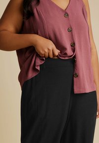 Lätt, mauve ärmlös topp med v-ringning och fyra mörka knappar; tillsammans med högmidjade svarta byxor med en jämn textur.