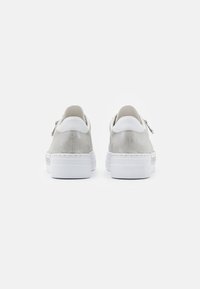 Sneakers med en mjuk, ljusgrå mocka ovandel och vita läderdetaljer. Har en tjock vit gummisula och sidodragkedja.