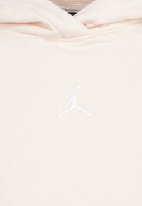 Kremeni dukserica s mekim teksturom, s bijelim Jumpman logotipom sprijeda. Dizajn uključuje kapuljaču s vezicom i rebraste manšete.