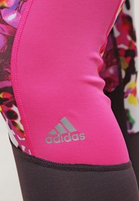Primer plano de pantalones deportivos Adidas en color rosa y negro con un patrón floral y el logo de Adidas visible en la sección de tela rosa.