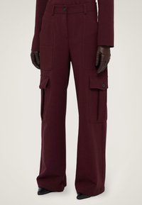 Bordeaux cargobroek met brede pijpen, gemaakt van een katoenmix, met zijzakken en drukknoopsluitingen. Gecombineerd met aansluitende bruine leren handschoenen.