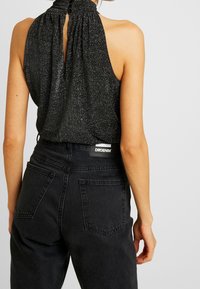 Haut noir à col licou avec un col froncé et un dos ajouré, associé à un jean en denim noir taille haute avec poches arrière et étiquette.