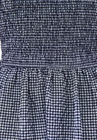 Ruudullinen mekko, jossa on tummansininen ja valkoinen ruudukko, smokkikirjailtu yläosa ja kerrostettu hame, joka tuo tekstuuria ja liikettä.