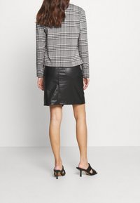 Blazer a cuadros en blanco y negro combinado con una falda de cuero negra. El conjunto presenta mangas largas, un diseño estructurado y una silueta ajustada.