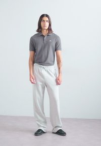 Gray polo shirt with a logo, paired with light gray, drawstring sweatpants. The model wears black slip-on shoes. Simple, casual style.