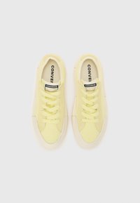 Kollane canvas-sneakerid tekstuurse viimistlusega, ümar varvas ja kreemvalge kummitald. Omab paelu ja musta silti keelega.