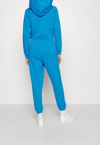 Blå huvtröja och matchande joggingsbyxor i mjukt tyg. Joggingsbyxorna har elastiska muddar och midja. Bärs med vita sneakers.