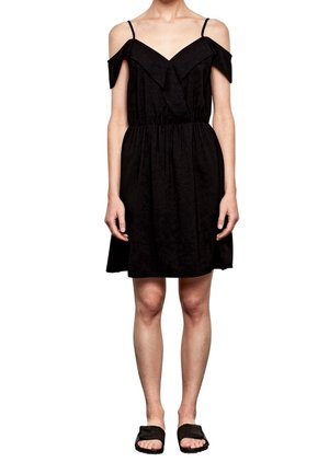 Robe noire décolletée avec des bretelles fines, corsage en couches, taille élastique et jupe évasée ; portée avec des sandales noires plates.