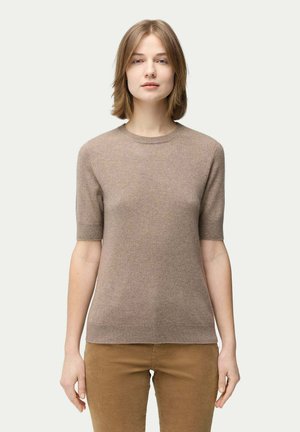 Pull ajusté à manches courtes de couleur marron clair, en tissu doux, avec un col rond et des poignets côtelés. Porté avec un pantalon beige.