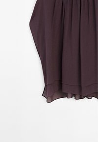 Jupe superposée violet foncé avec un ourlet asymétrique et un tissu léger sur fond blanc.
