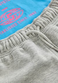 Lys grå sweatpants med tekstureret talje og snøre, parret med en blå t-shirt med rosa grafisk tekst og logo.