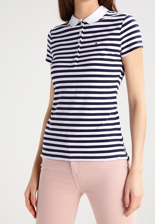 Femme portant un polo à manches courtes rayé bleu marine et blanc associé à un pantalon rose clair, debout, les bras détendus le long du corps.