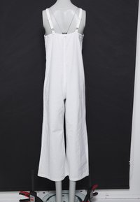 Combinaison en lin blanc avec un design à jambes larges, bretelles réglables et fermeture dos par boutons. Texture lisse, apparence minimaliste.