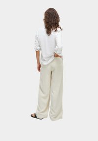 Wijde lichtbeige broeken met een gladde textuur, gecombineerd met een witte button-up shirt. Het shirt heeft opgerolde mouwen en een ontspannen pasvorm.