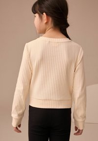 Cremeförmiger Rippstrickpullover mit langen Ärmeln, Rundhalsausschnitt und enganliegendem Saum. Getragen mit schwarzen Rippstrickhosen. Einfaches, strukturiertes Design.
