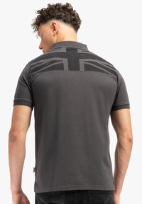 Šedé polo tričko s texturovaným černým designem Union Jack na zadní straně. Krátké rukávy a klasický límeček. Měkký materiál z bavlněné směsi.