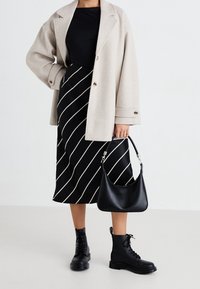 Beige villasekoite-takki, musta paita, mustavalkoraidallinen midihame. Mustat nahkaiset korolliset taistelukengät ja musta olkalaukku, jossa metalliyksityiskohdat.